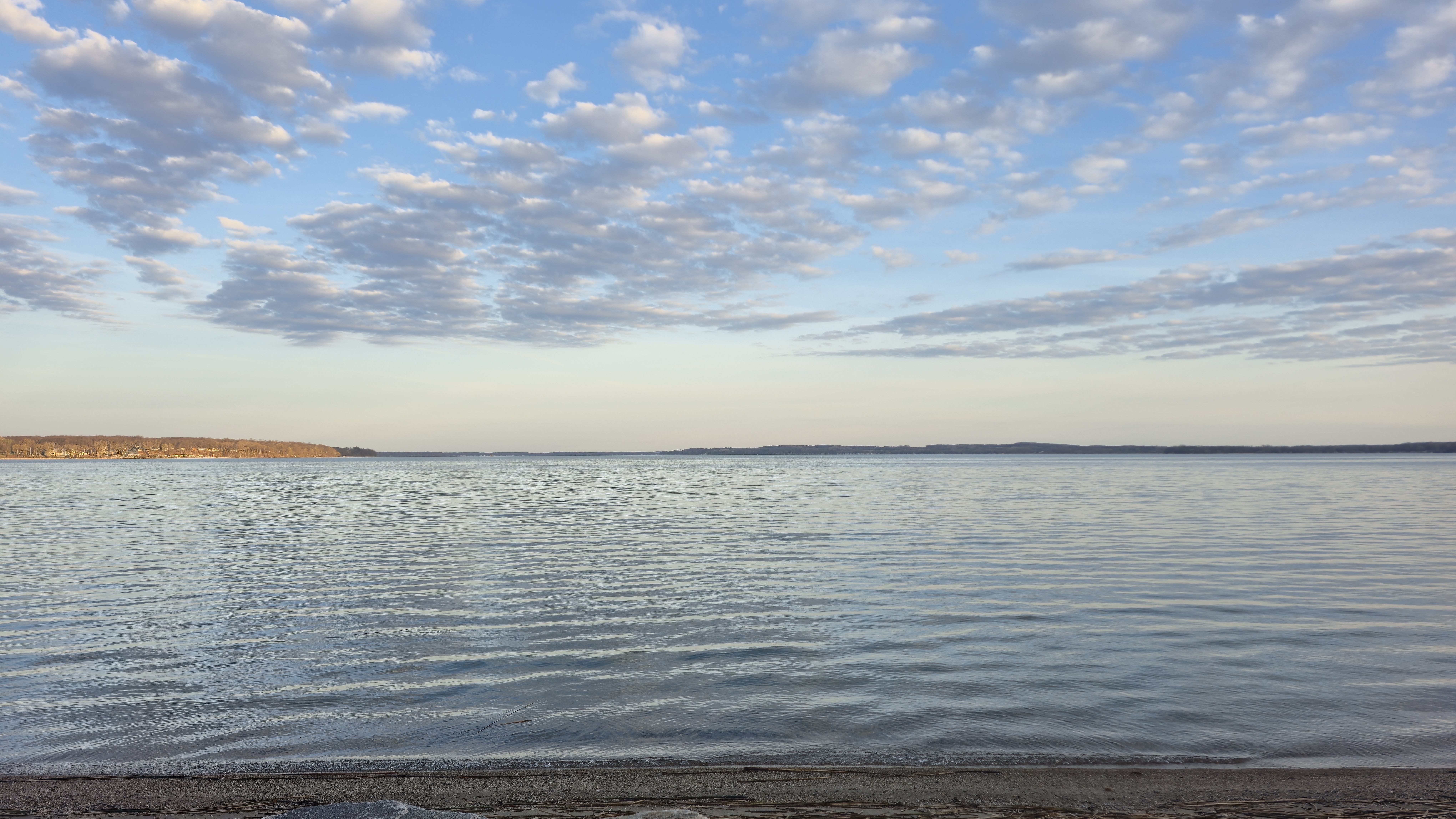 A calm body of water reflects a blue sky with scattered clouds.